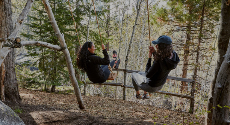 Two women swinging on swings in the forest