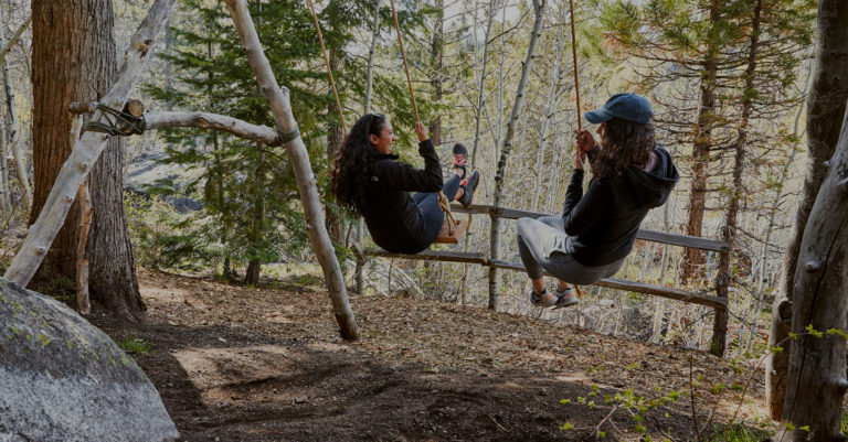 Two women swinging on swings in the forest