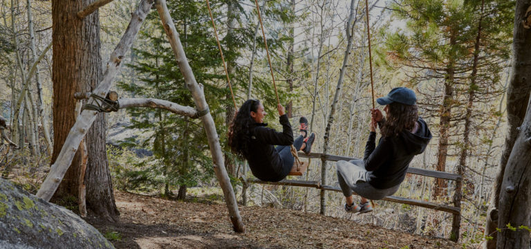 Two women swinging on swings in the forest