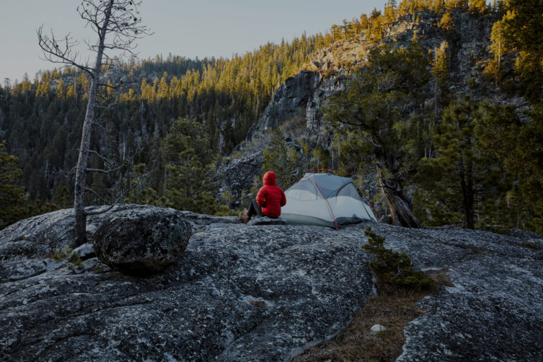 Tent on top of a large boulder with person sitting next to it looking out