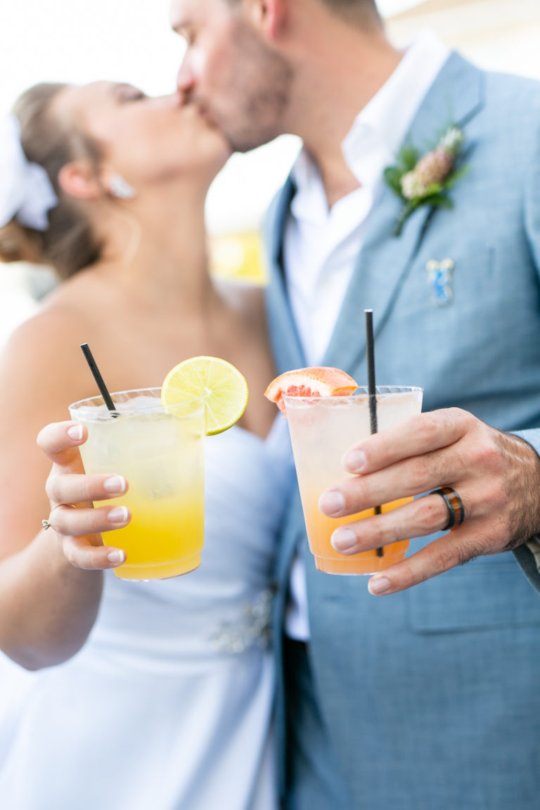 Bride and groom holding cocktails kissing